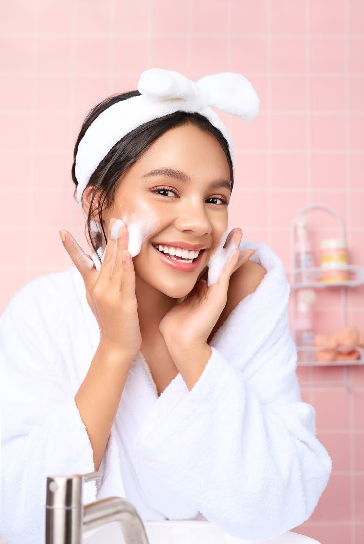 Woman applying cream to her face with a pink background